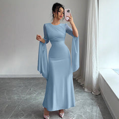 Woman in a light blue dress taking a mirror selfie in a room with a window and white curtains.